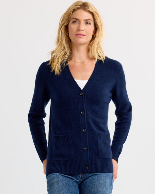 Woman wearing navy cashmere cardigan with buttons and front pockets, paired with blue jeans and white top underneath