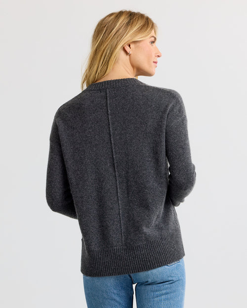 LIFESTYLE / EDITORIAL: Woman wearing dark grey cashmere sweater and blue jeans, viewed from back against plain background