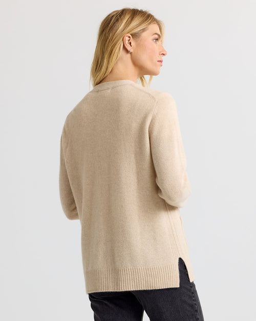 LIFESTYLE / EDITORIAL: Woman wearing a sandstone beige cashmere sweater, viewed from the back against a plain background