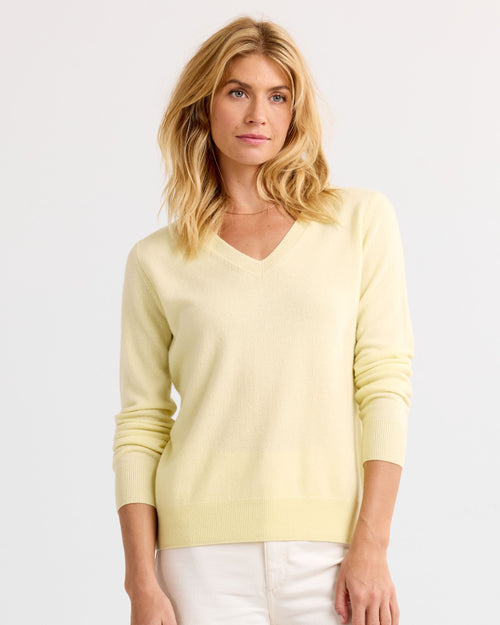 Woman wearing buttermilk yellow V-neck cashmere sweater, standing against plain light background