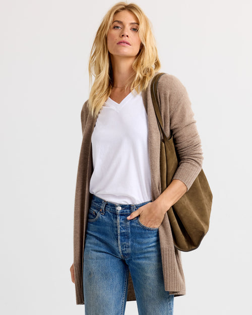 LIFESTYLE / EDITORIAL: Woman wearing white V-neck tee, driftwood-colored long cardigan, blue jeans, and carrying a brown