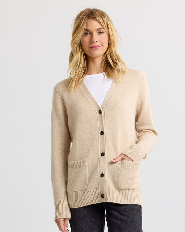 Woman wearing sandstone beige cashmere cardigan with front pockets and black buttons over white top