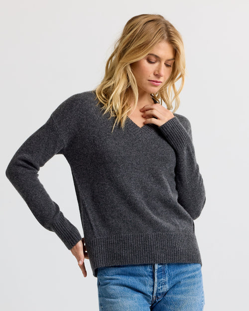 LIFESTYLE / EDITORIAL: Woman wearing dark grey V-neck cashmere sweater and blue jeans, posing against a plain background