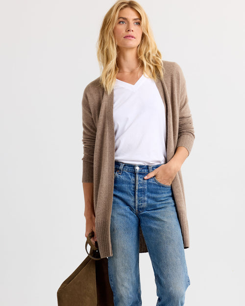LIFESTYLE / EDITORIAL: Woman wearing driftwood-colored long cashmere cardigan, white V-neck tee, and blue jeans holding a bag