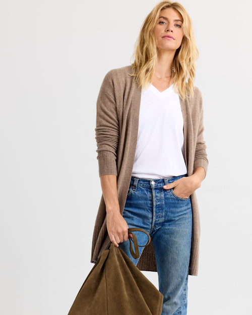 LIFESTYLE / EDITORIAL: Woman wearing driftwood brown long cashmere cardigan, white V-neck shirt, blue jeans, holding olive