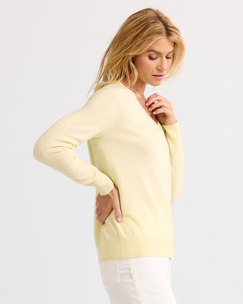 Woman in side profile wearing a buttermilk-colored V-neck cashmere sweater and white pants against a white background