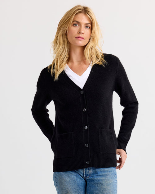 Front view image of a woman wearing a black buttoned cashmere cardigan over a white V-neck shirt and blue jeans