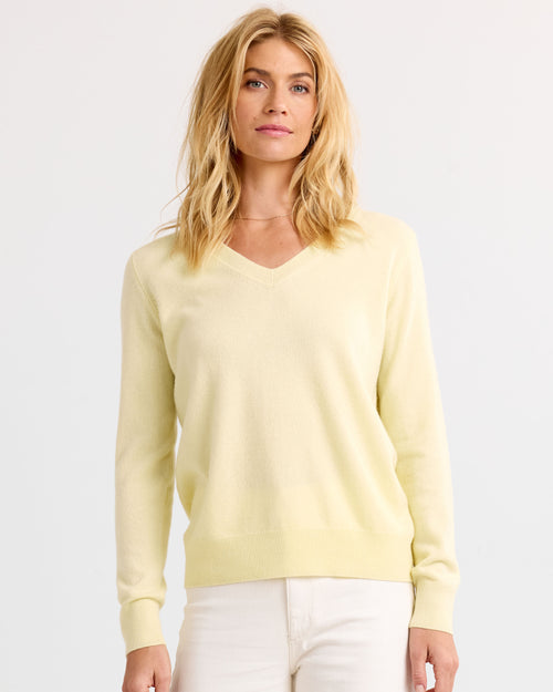 Front-facing image of a woman wearing a buttermilk yellow V-neck cashmere sweater and white pants