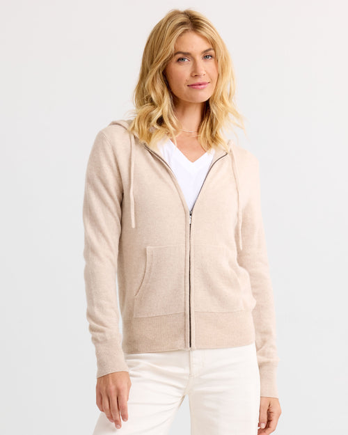 LIFESTYLE / EDITORIAL: Woman wearing oatmeal zip-up cashmere hoodie and white pants against plain background