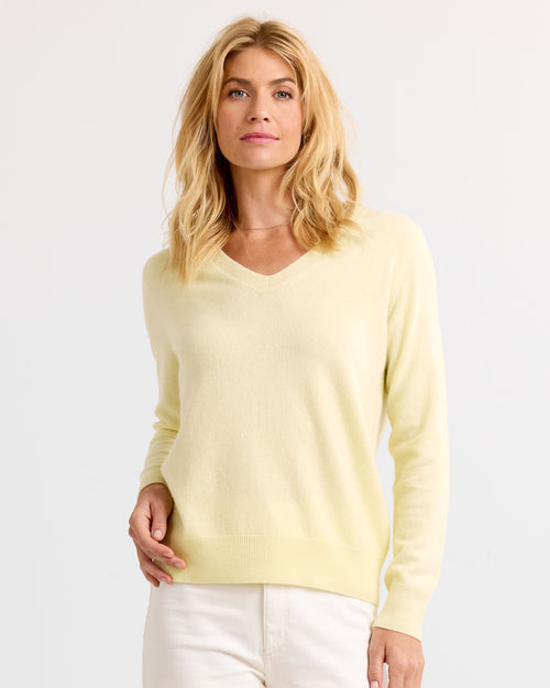 Front view image of a woman wearing a light yellow V-neck cashmere sweater and white pants against a plain background