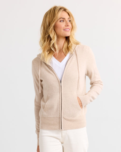 LIFESTYLE / EDITORIAL: Woman wearing oatmeal zip-up cashmere hoodie and white pants, looking to side against white background