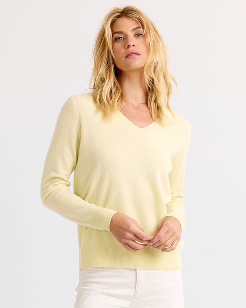 Woman wearing a buttermilk yellow V-neck cashmere sweater, standing against a plain white background