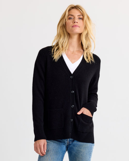 Front view image of a woman wearing black buttoned cashmere cardigan with pockets over white top and blue jeans