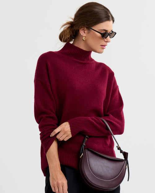 LIFESTYLE / EDITORIAL: Woman wearing barolo red cashmere turtleneck sweater, holding matching leather handbag, sunglasses on