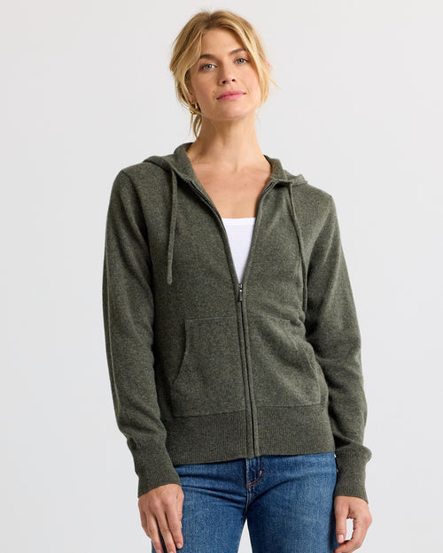 LIFESTYLE / EDITORIAL: Woman wearing dark olive zip-up cashmere hoodie with hood and front pockets, paired with blue jeans