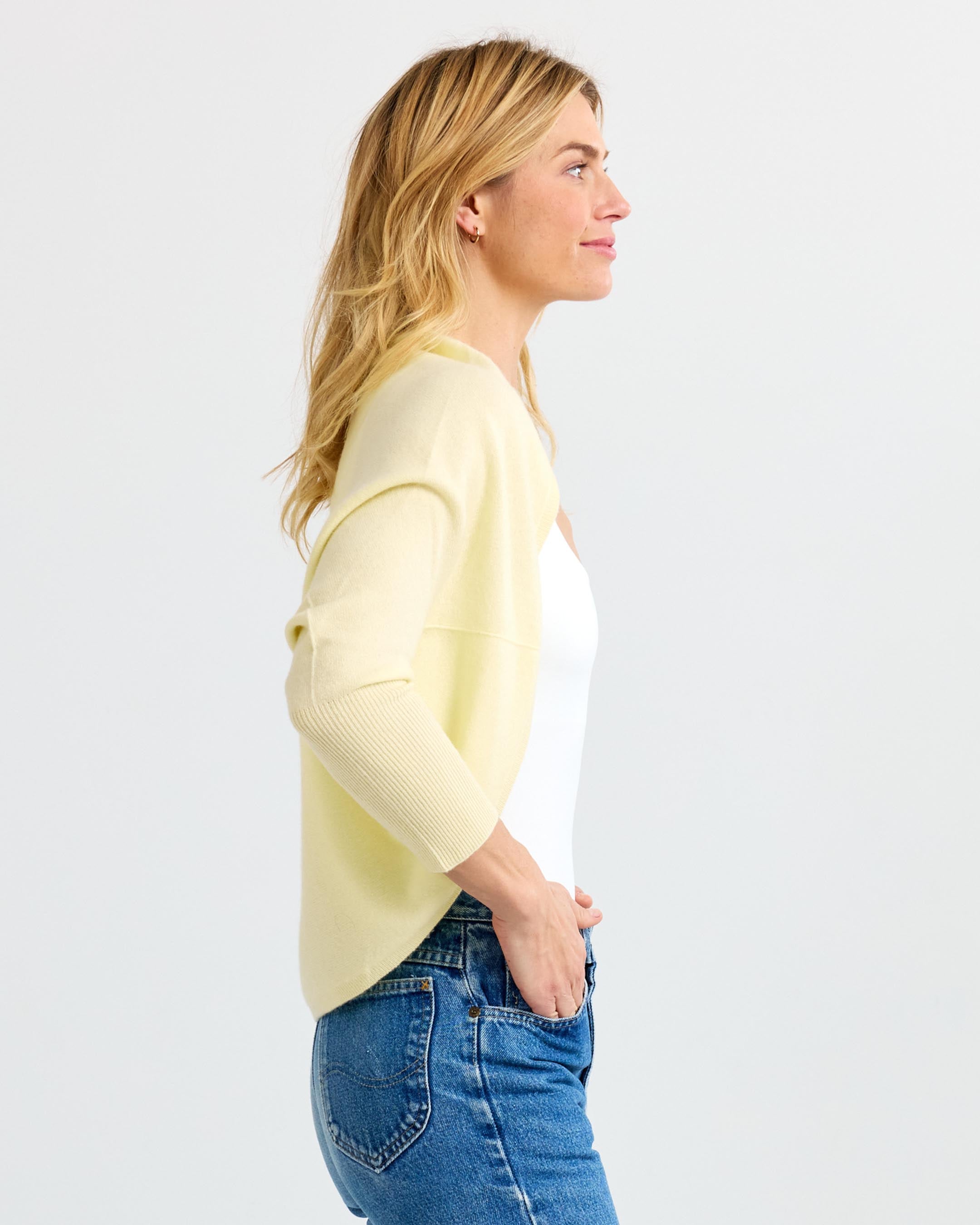 LIFESTYLE / EDITORIAL: Woman in side profile wearing a light yellow cashmere cardigan and blue jeans against white background