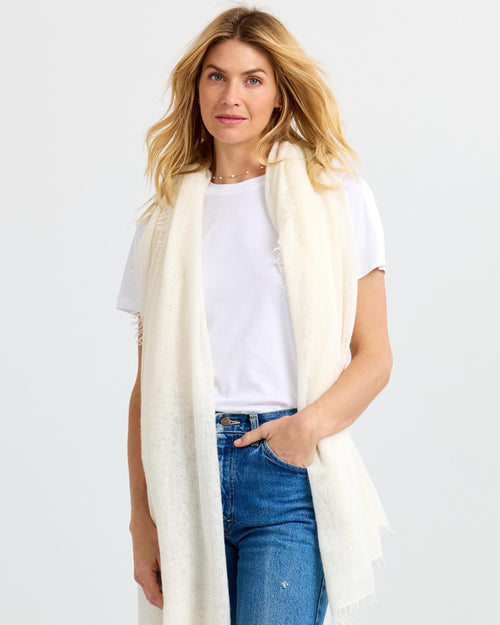 LIFESTYLE / EDITORIAL: Woman wearing white cashmere scarf, white t-shirt, and blue jeans against plain background