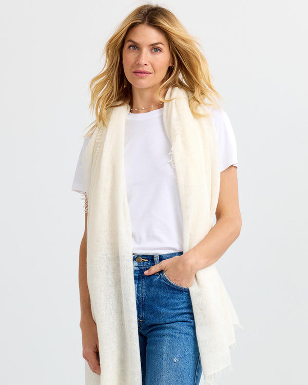 LIFESTYLE / EDITORIAL: Woman wearing white cashmere scarf, white t-shirt, and blue jeans against plain background