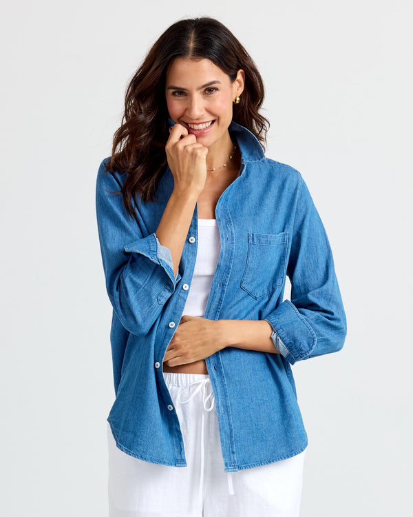 LIFESTYLE / EDITORIAL: Woman wearing medium wash denim shirt over white outfit, smiling against plain background
