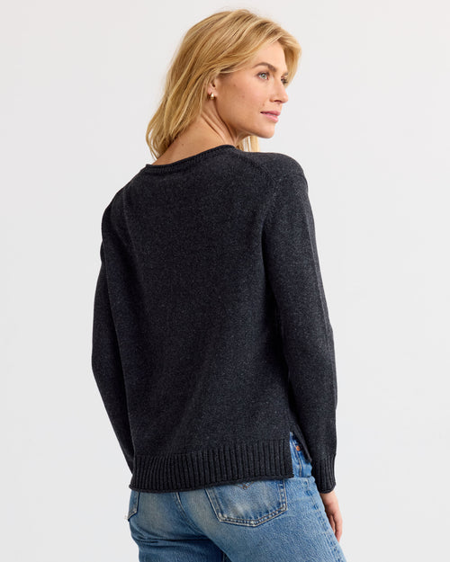 Back view image of a woman wearing a charcoal cashmere sweater paired with blue jeans, looking to the side.
