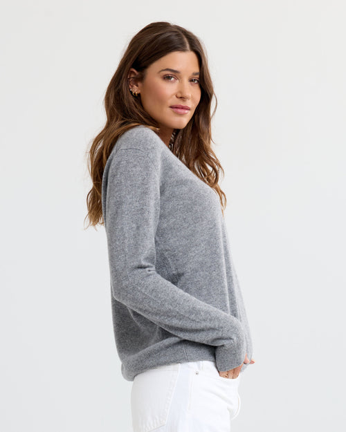 LIFESTYLE / EDITORIAL: Woman wearing grey cashmere sweater and white pants, standing sideways against white background