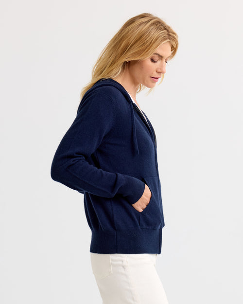 LIFESTYLE / EDITORIAL: Woman in navy cashmere hoodie and white pants, side profile against plain background