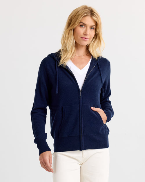 LIFESTYLE / EDITORIAL: Woman wearing navy zip-up cashmere hoodie and white V-neck shirt against plain background