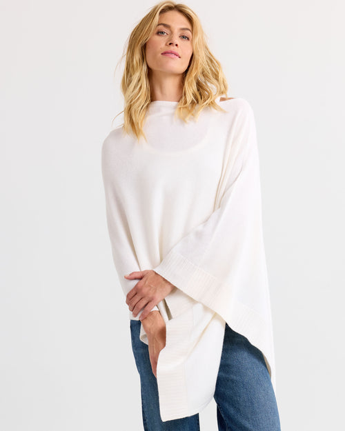 LIFESTYLE / EDITORIAL: Woman wearing ivory cashmere poncho with blue jeans against white background