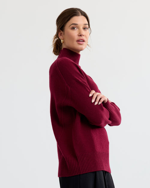 Woman in side profile wearing a barolo-colored turtleneck cashmere sweater with long sleeves and ribbed hem and cuffs