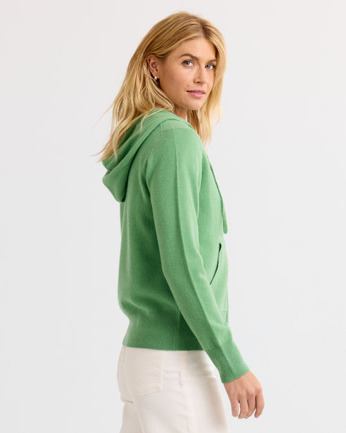 Woman wearing matcha green cashmere hoodie, side view, white pants, plain background