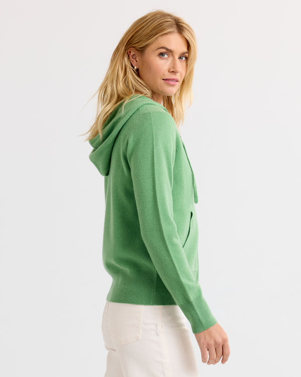 Woman wearing matcha green cashmere hoodie, side view, white pants, plain background