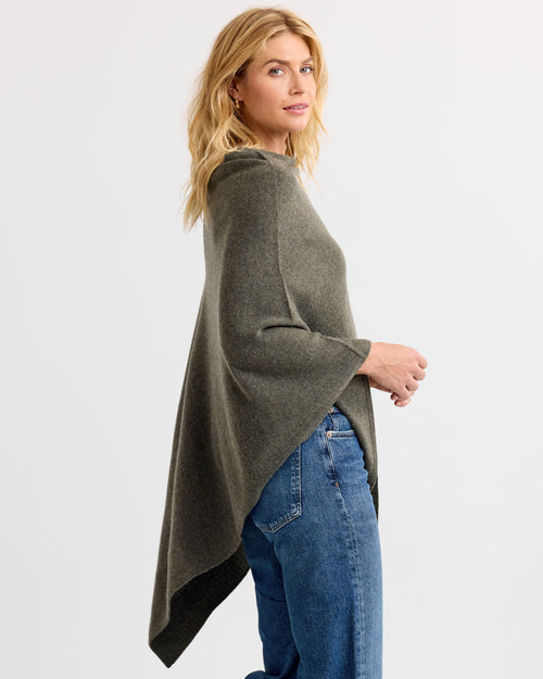 LIFESTYLE / EDITORIAL: Woman wearing dark olive cashmere poncho with jeans, side view against plain background