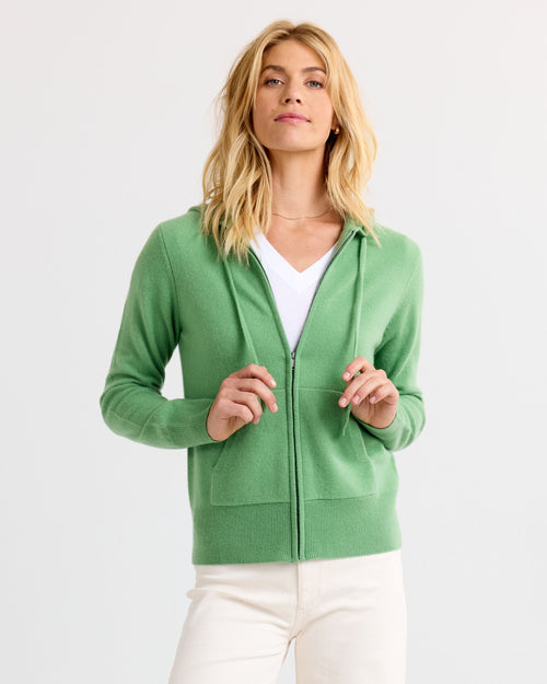 Woman wearing green zip-up cashmere hoodie over white V-neck shirt, standing against white background