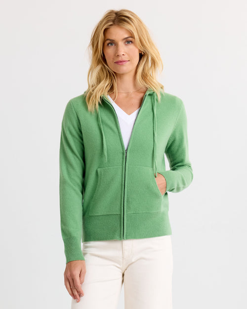 LIFESTYLE / EDITORIAL: Woman wearing green zip-up cashmere hoodie and white pants against plain white background