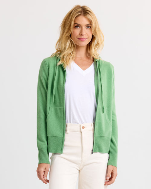 Woman wearing light green zip-up cashmere hoodie and white V-neck shirt against white background