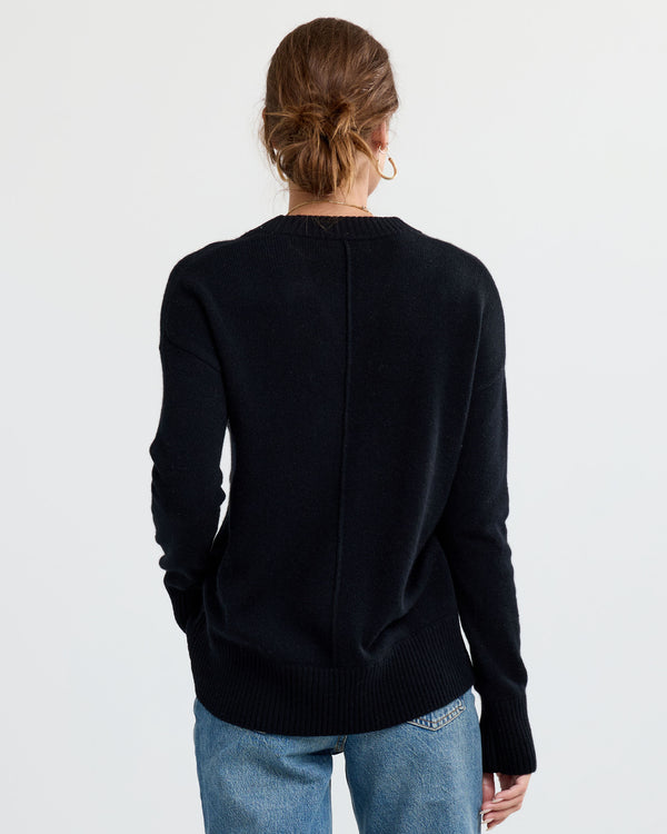 Rear view image of a woman wearing a black cashmere sweater and blue jeans with hair tied up against white backdrop
