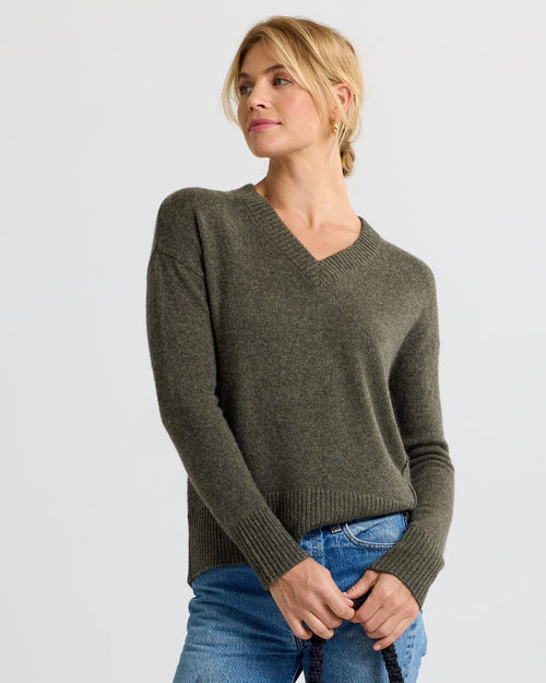 Woman wearing olive green V-neck cashmere sweater and blue jeans against plain background