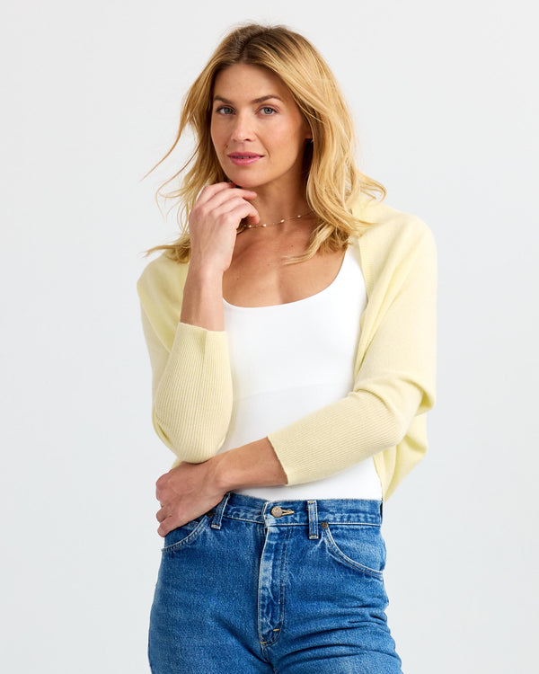 LIFESTYLE / EDITORIAL: Woman wearing buttermilk yellow cashmere shrug over white top and blue jeans against white background