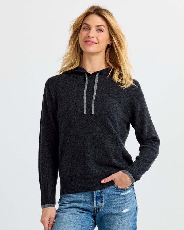LIFESTYLE / EDITORIAL: Woman wearing charcoal gray cashmere hoodie and blue jeans, standing against white background