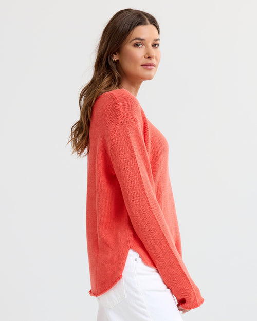 LIFESTYLE / EDITORIAL: Woman in coral cashmere sweater and white pants, side view against plain background
