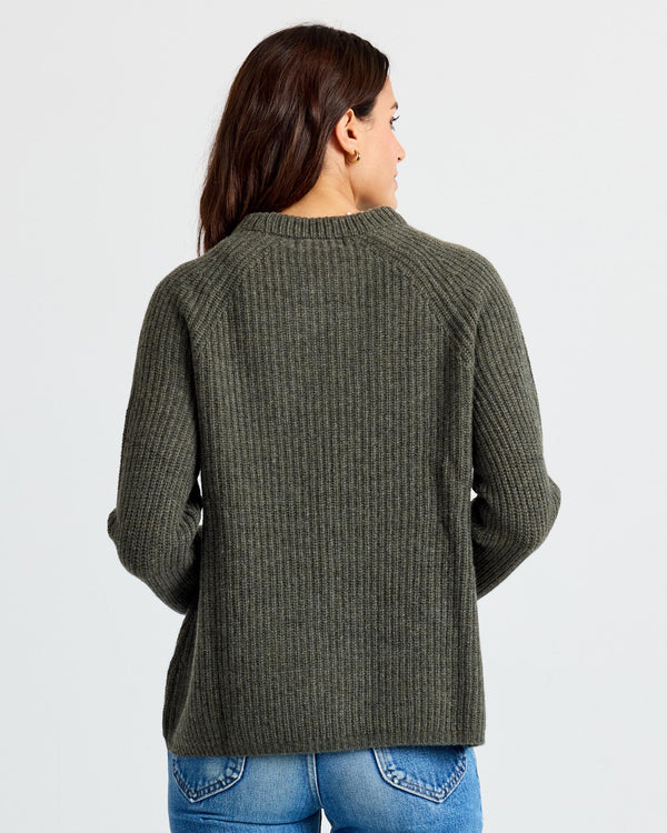 LIFESTYLE / EDITORIAL: Woman wearing dark olive ribbed cashmere sweater, back view, paired with blue jeans against white