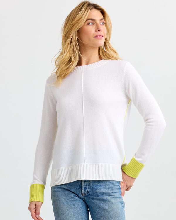LIFESTYLE / EDITORIAL: Woman wearing white cashmere sweater with yellow cuffs and blue jeans, standing against white