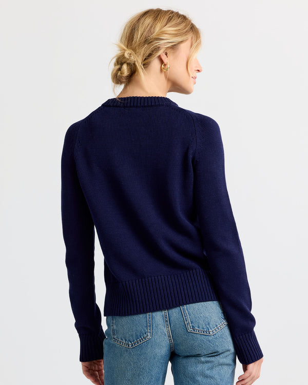 Woman wearing navy cashmere sweater and blue jeans, shown from the back against a plain light background