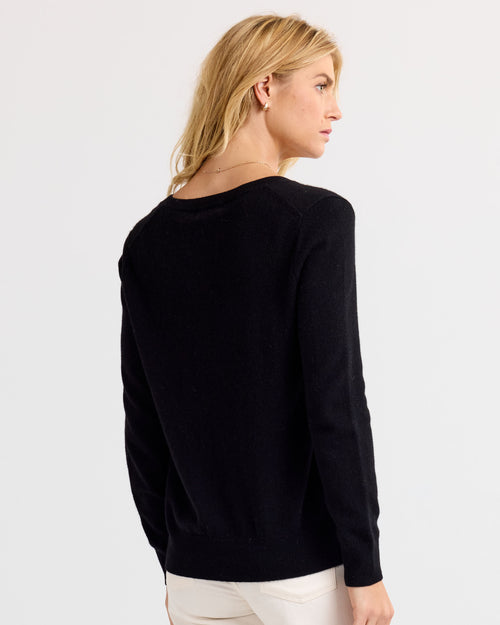 Woman wearing black cashmere sweater, shown from back, standing against plain light background