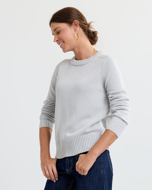 LIFESTYLE / EDITORIAL: Woman in light grey cashmere sweater and dark jeans, smiling with hair tied back