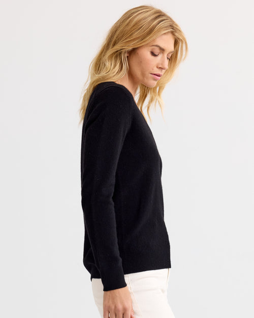 LIFESTYLE / EDITORIAL: Woman in black cashmere sweater and white pants, side profile against plain background