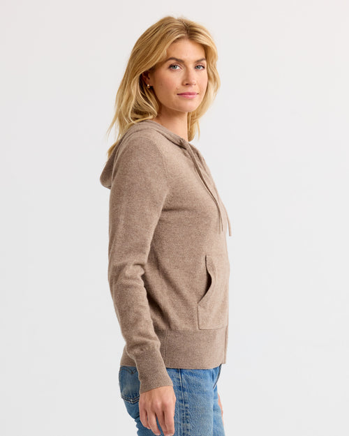 LIFESTYLE / EDITORIAL: Woman in driftwood-colored cashmere hoodie and jeans, side profile against plain background