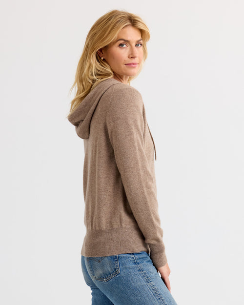 LIFESTYLE / EDITORIAL: Woman wearing driftwood-colored cashmere hoodie and jeans, standing sideways against white background