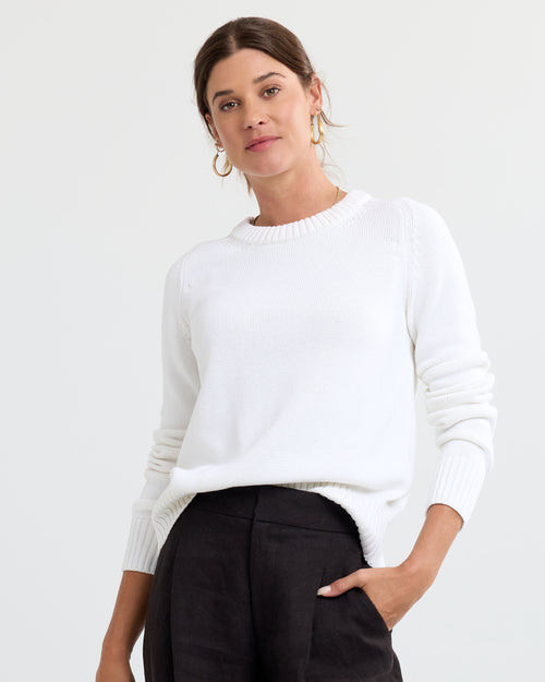 LIFESTYLE / EDITORIAL: Woman wearing cream cashmere sweater and black pants with hand in pocket against white background