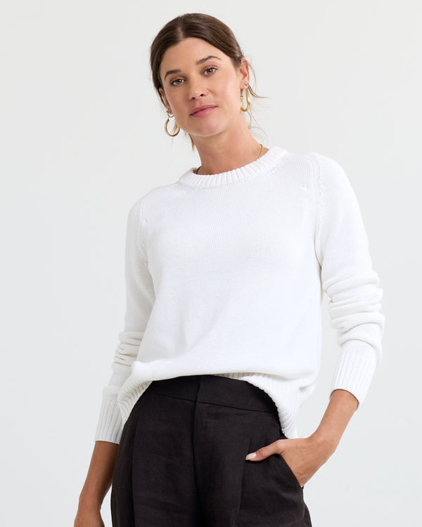 LIFESTYLE / EDITORIAL: Woman wearing cream cashmere sweater and black pants with hand in pocket against white background